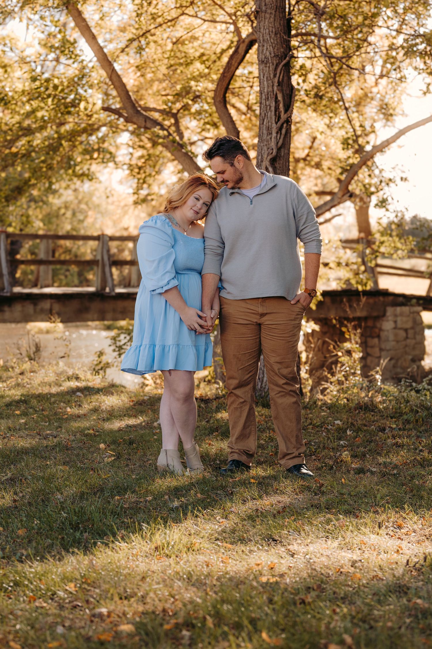 A couple shares a sweet moment together under trees in warm afternoon light.