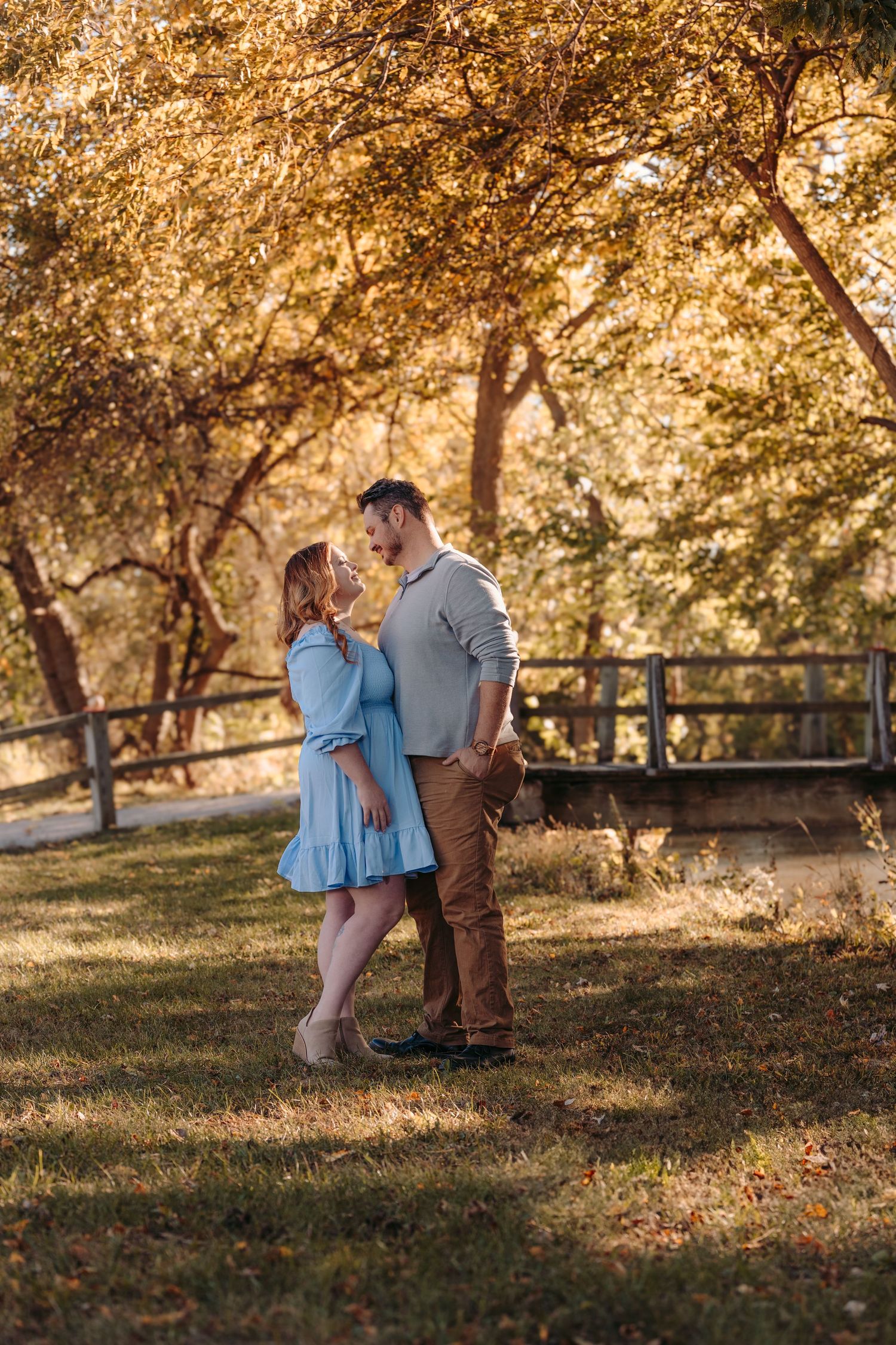 Couple standing together in a park with golden autumn trees and sunlight streaming through branches.