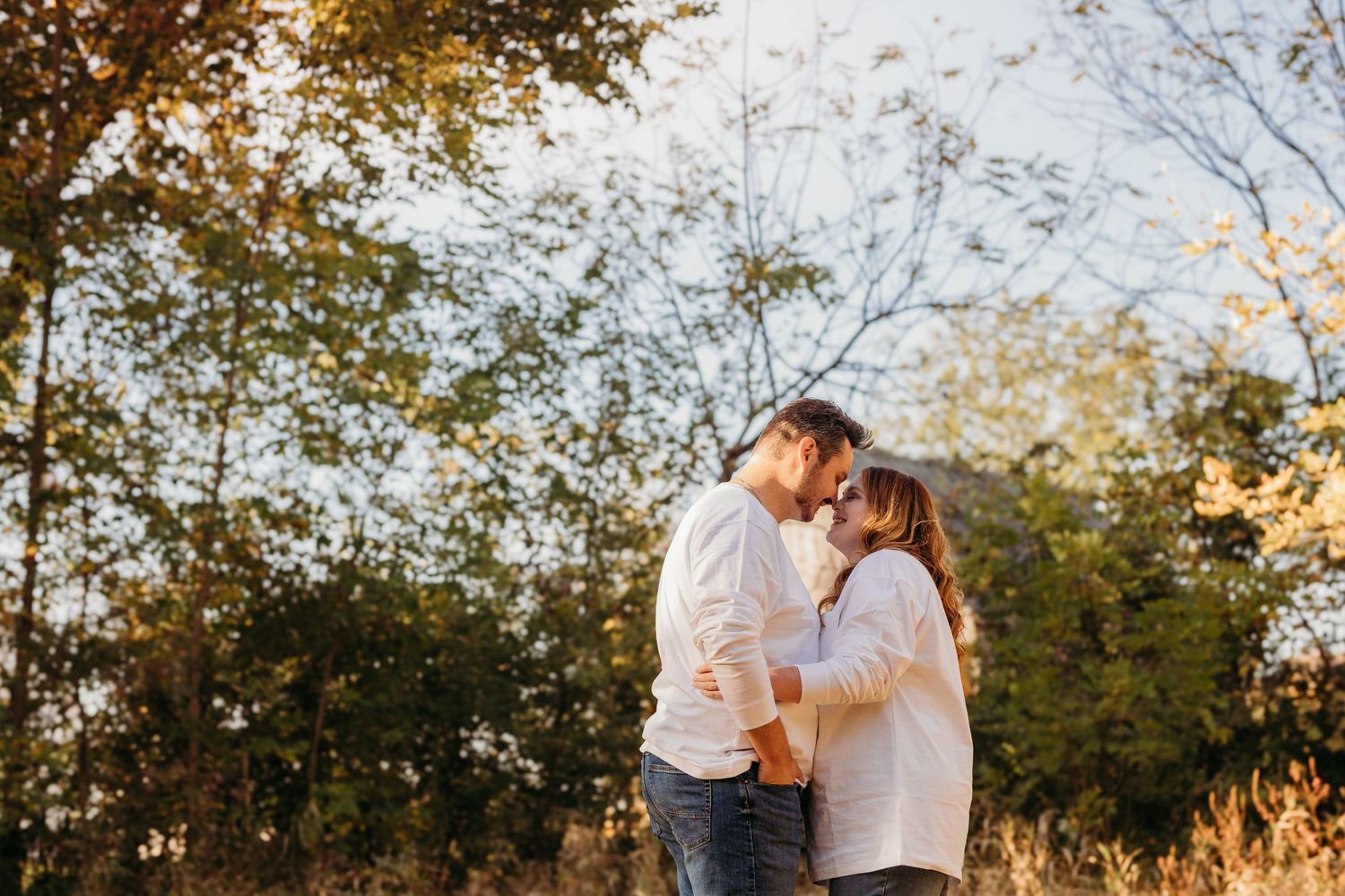 Couple sharing tender moment in autumn field during sunset.