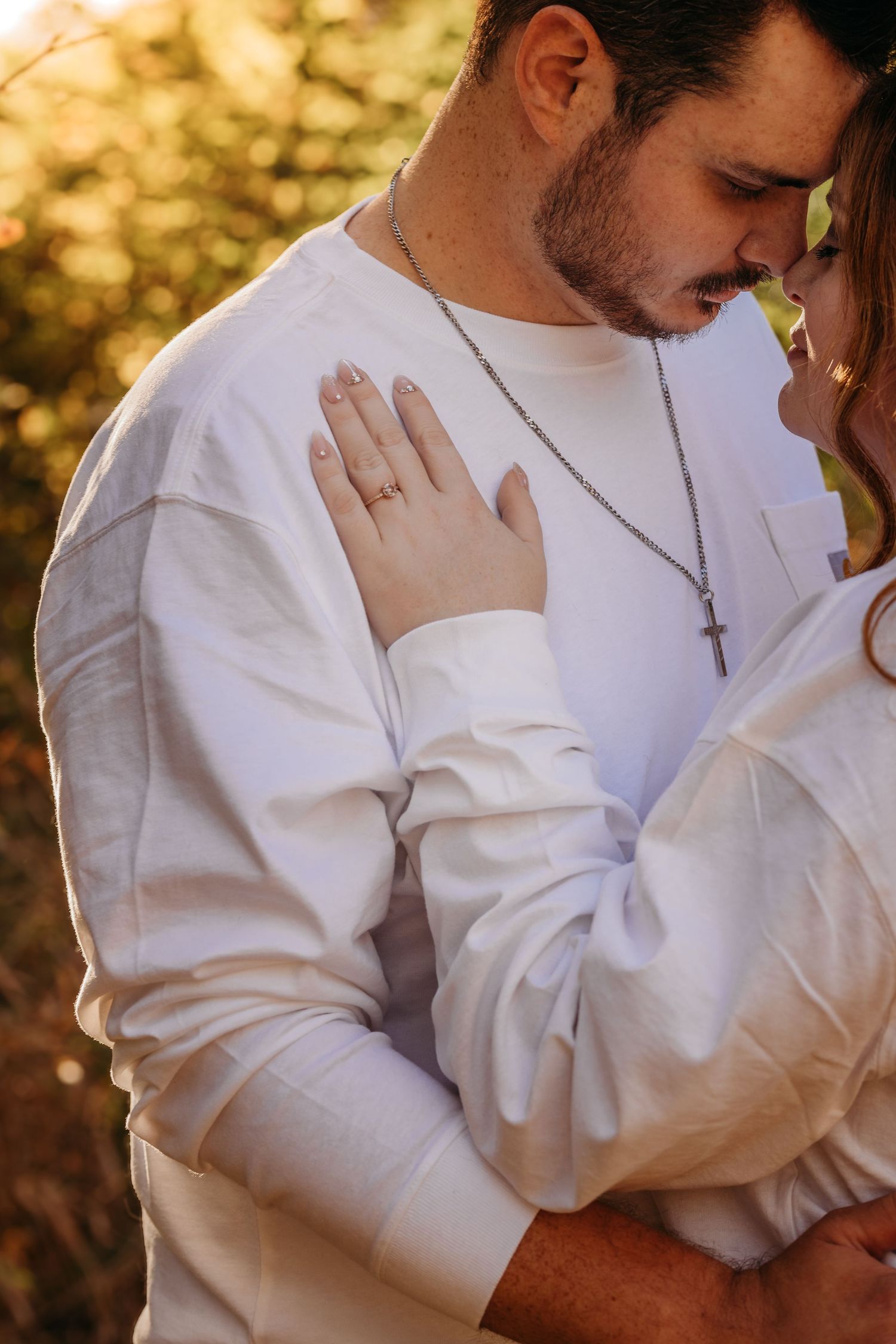 A close-up golden hour photo showing tender embrace between couple wearing matching white outfits.