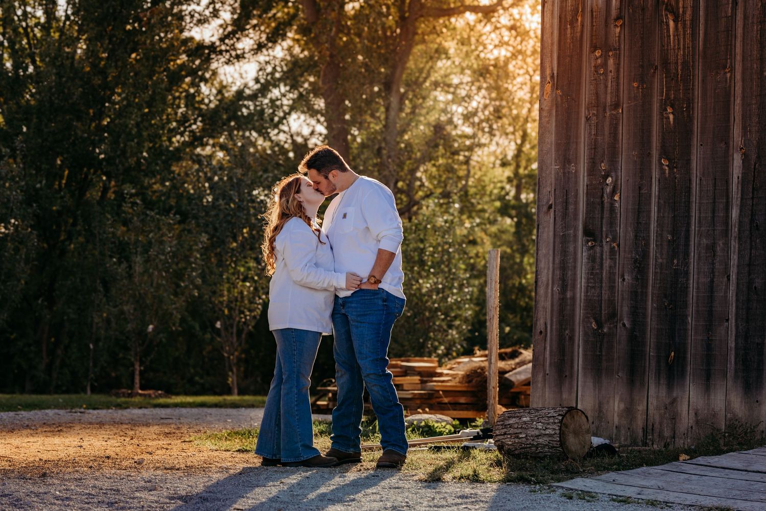 A romantic countryside photo session with couple in white and denim by wooden barn at sunset.