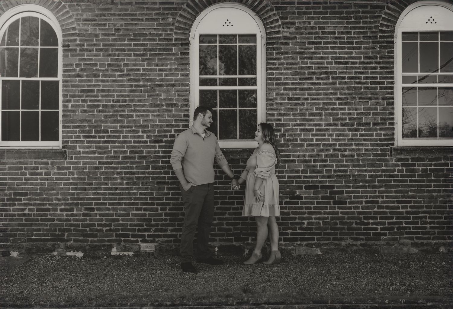 Vintage black and white portrait against brick building with arched windows.