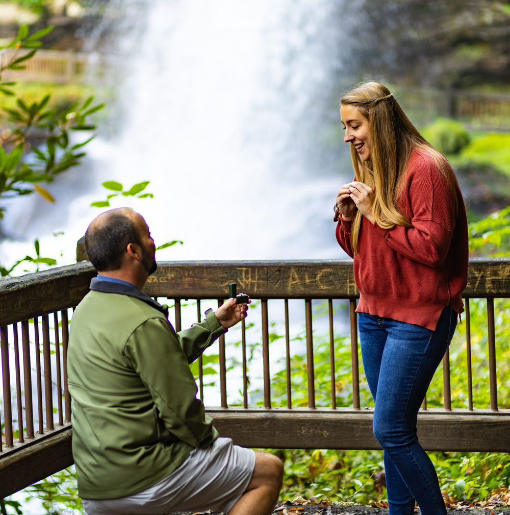 People leaning over wooden railing at a park to look at something in the distance while taking photos.