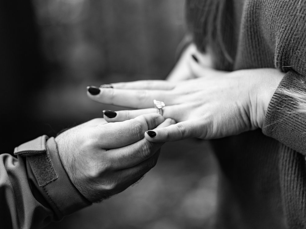 Two hands exchanging a pen or writing instrument, with black nail polish visible in black and white photography.