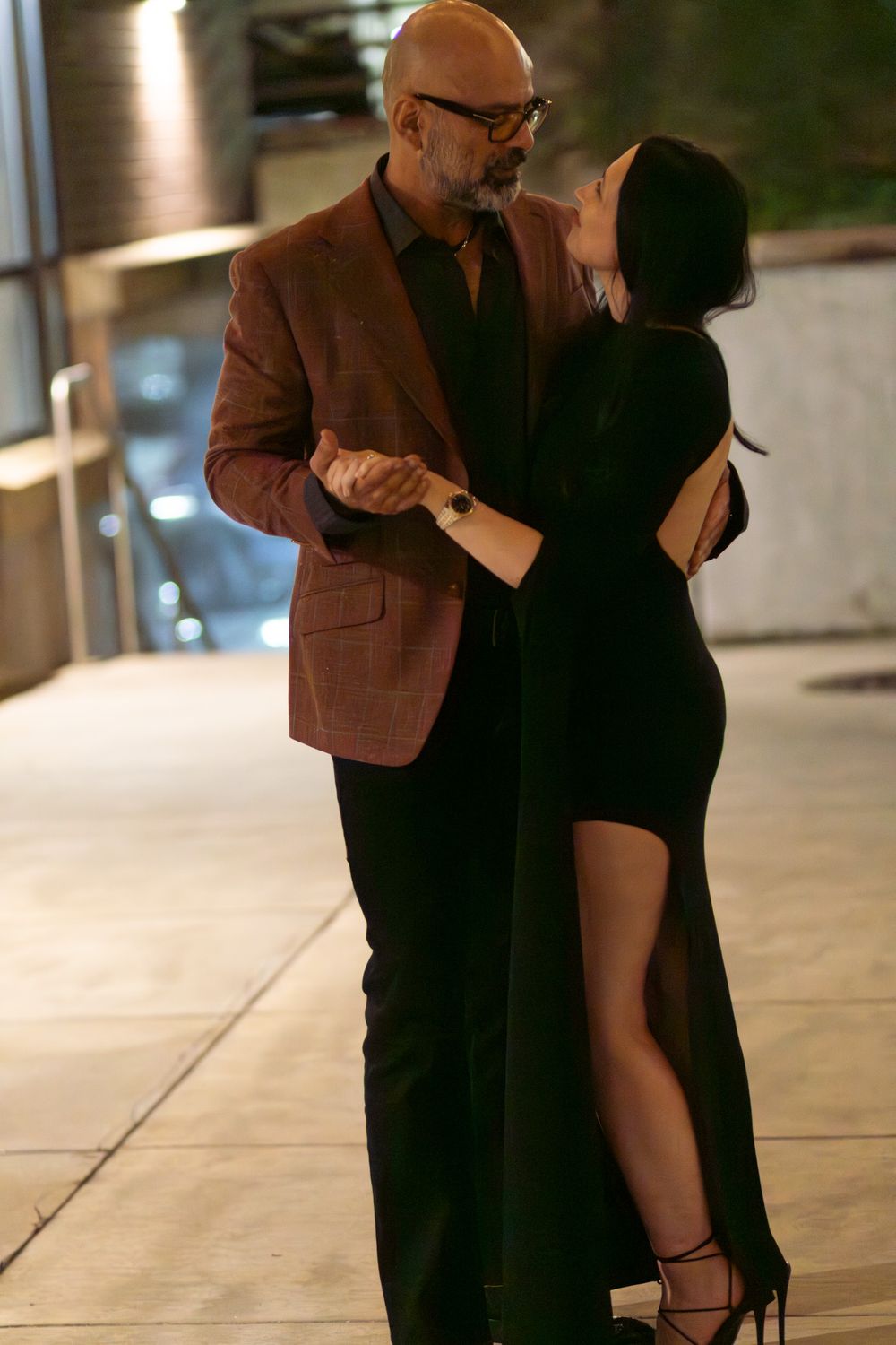 A couple in formal attire sharing an intimate moment during their engagement photo session on a city street at night.