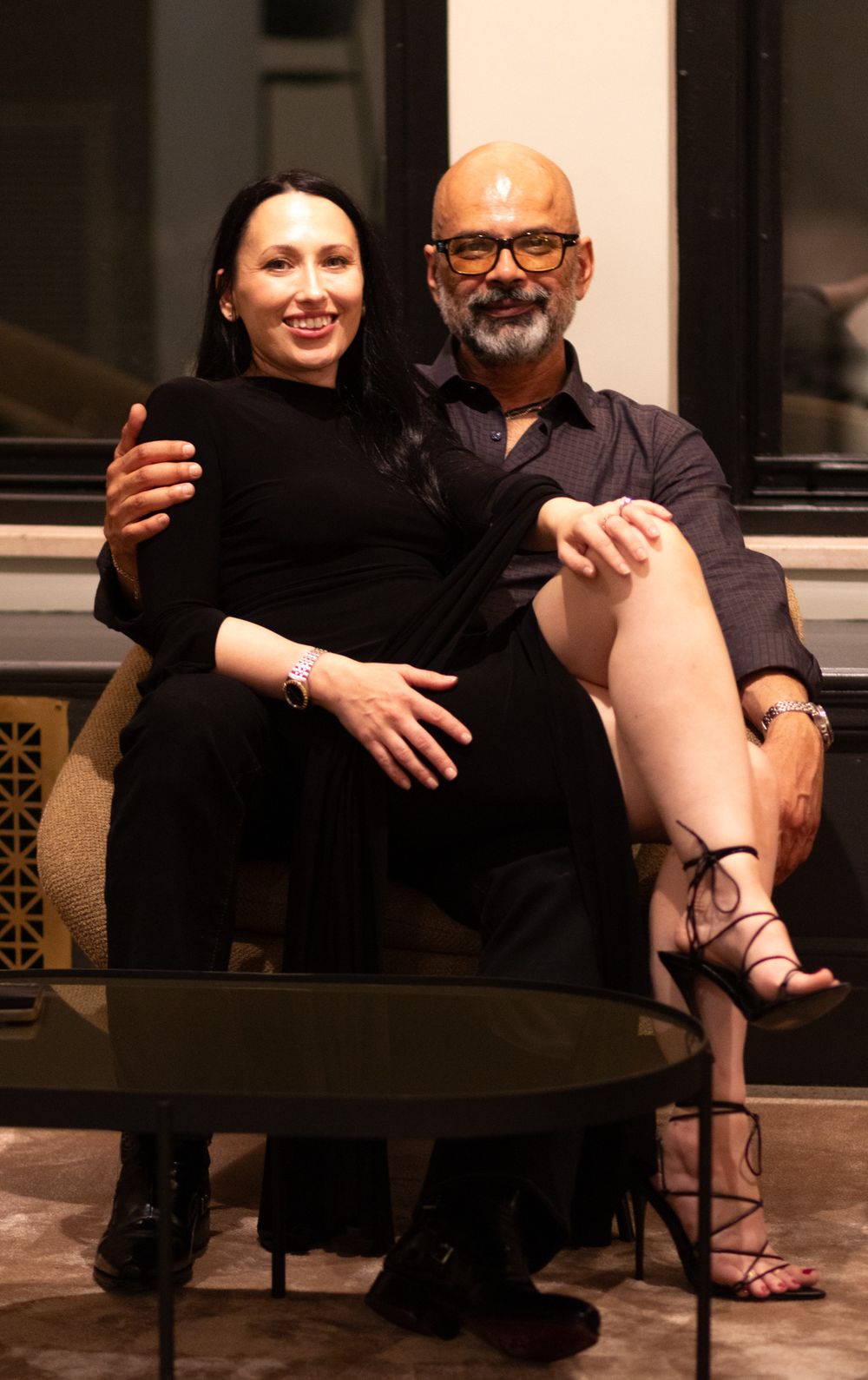 Two people in black clothing sit together on a couch in an intimate indoor setting.
