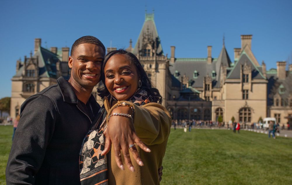 A couple poses in front of the stunning Biltmore Estate mansion on a sunny day.