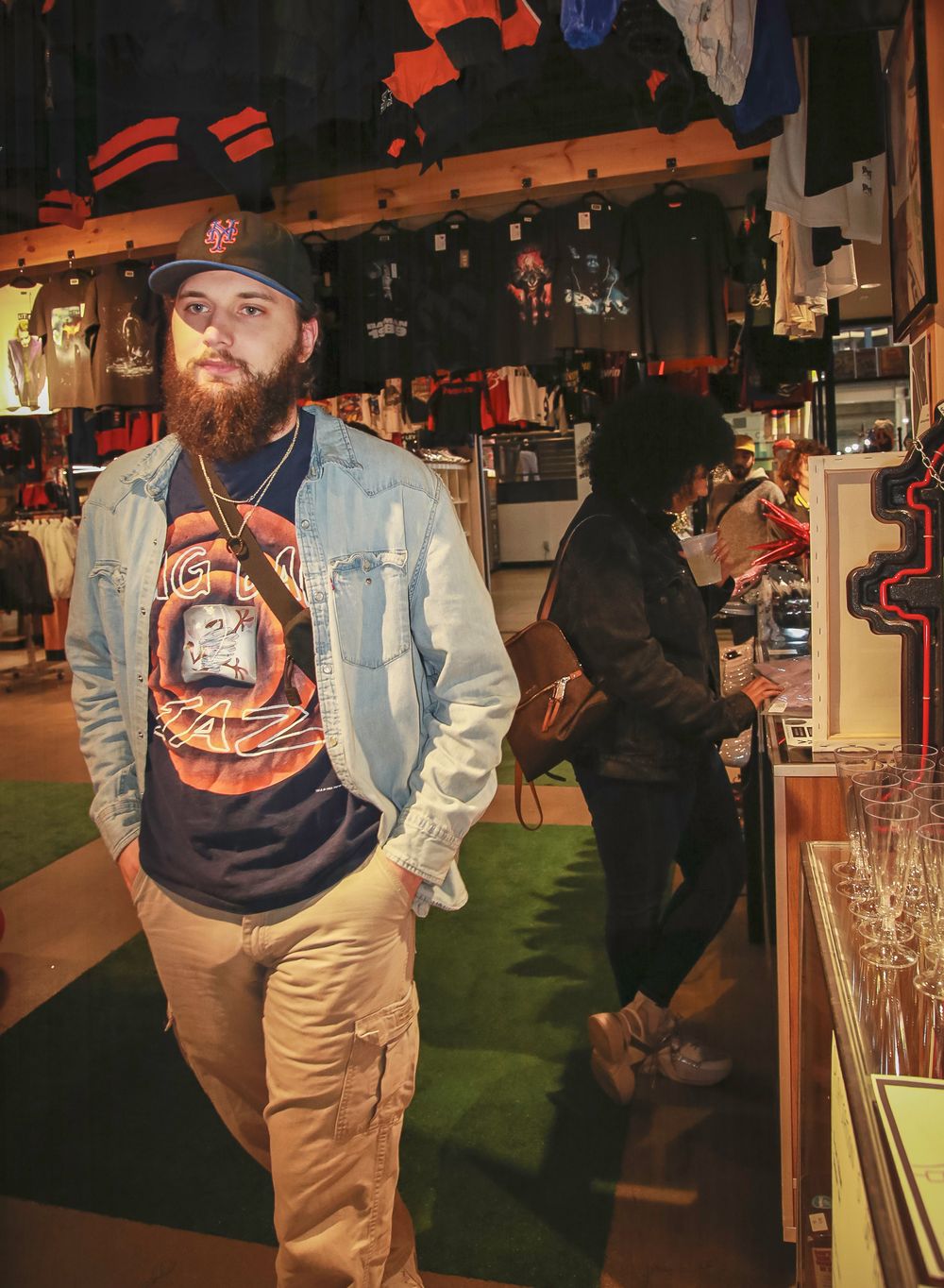 Person wearing a denim jacket and Star Wars t-shirt stands in a dimly lit bar with neon signs and decorative lighting.