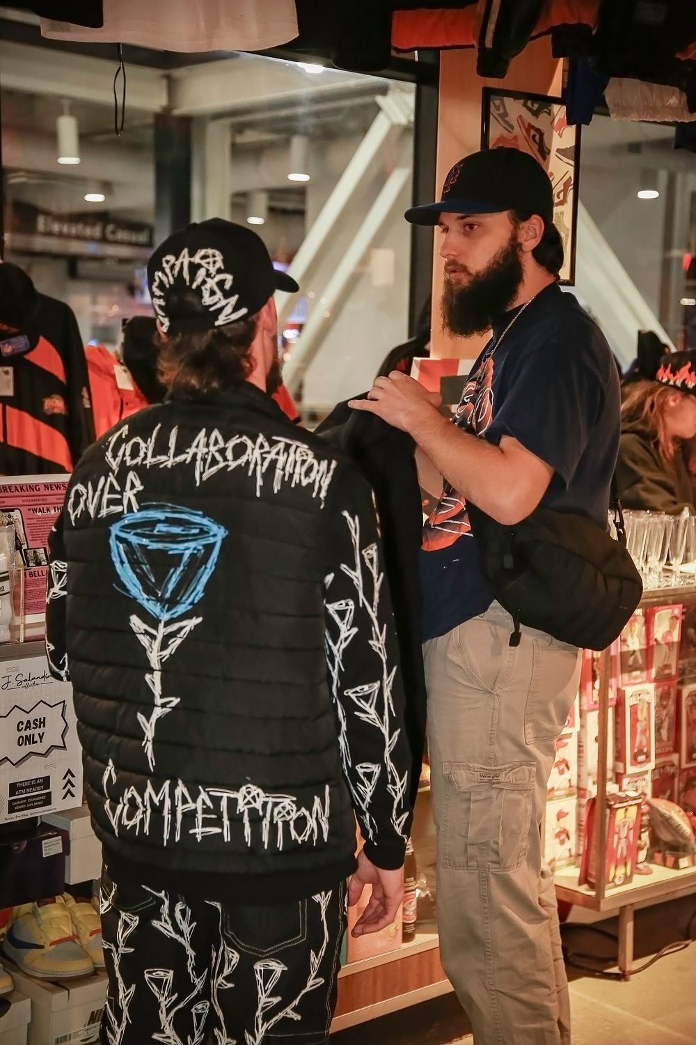 Two people in casual streetwear style clothing with black apparel and custom graphics inside a retail store setting.