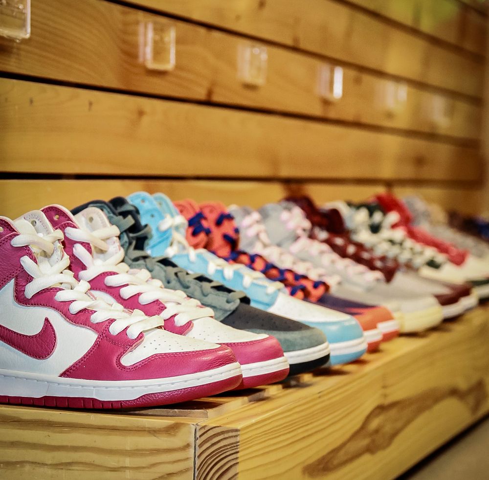 Row of colorful Nike Dunk sneakers displayed on wooden shelves featuring pink, blue and red color combinations.