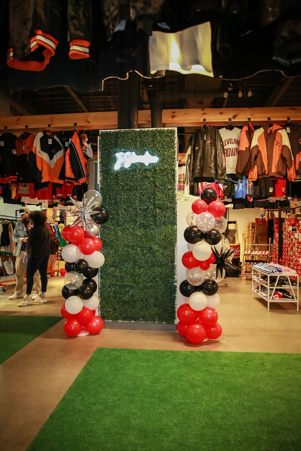 Retail store display with grass walls and red and black balloon decorations at entrance.