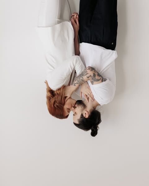 A couple in white clothing lying on a white floor in an artistic overhead shot.