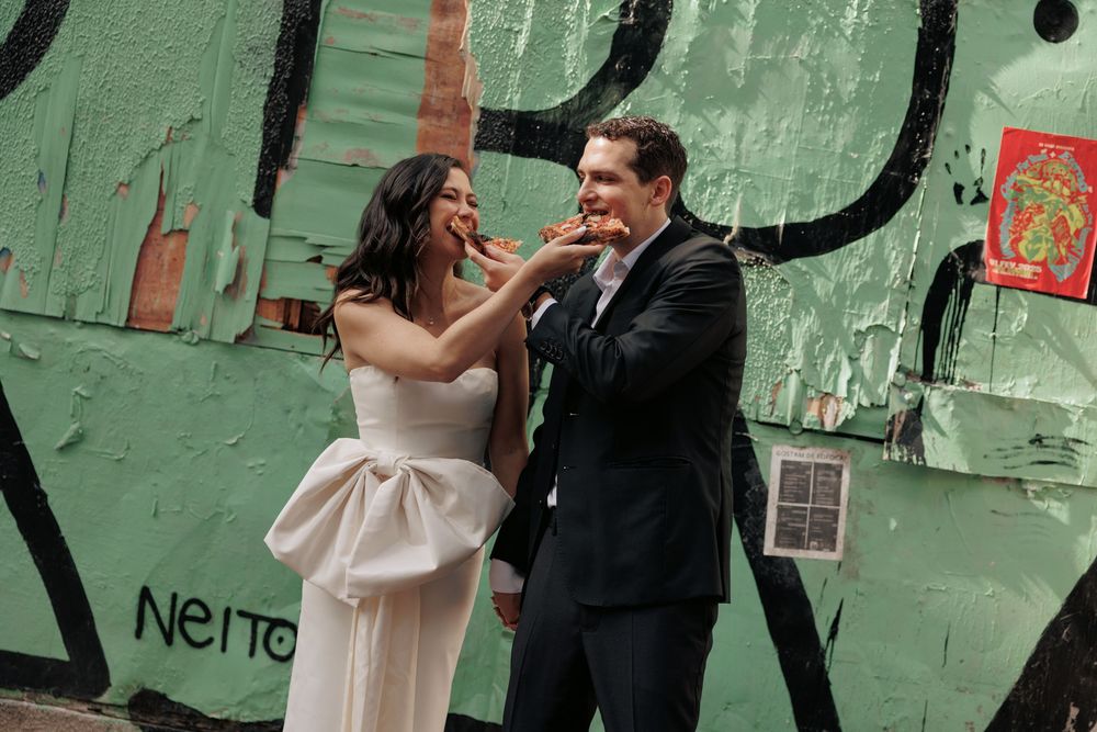 A joyful wedding moment against a green graffiti wall with a bride in a strapless dress and groom in black suit.