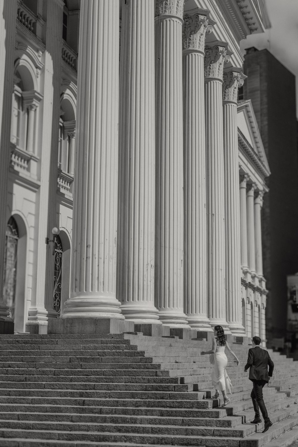 Classical columns and stone steps lead up to a grand building entrance in black and white photography.