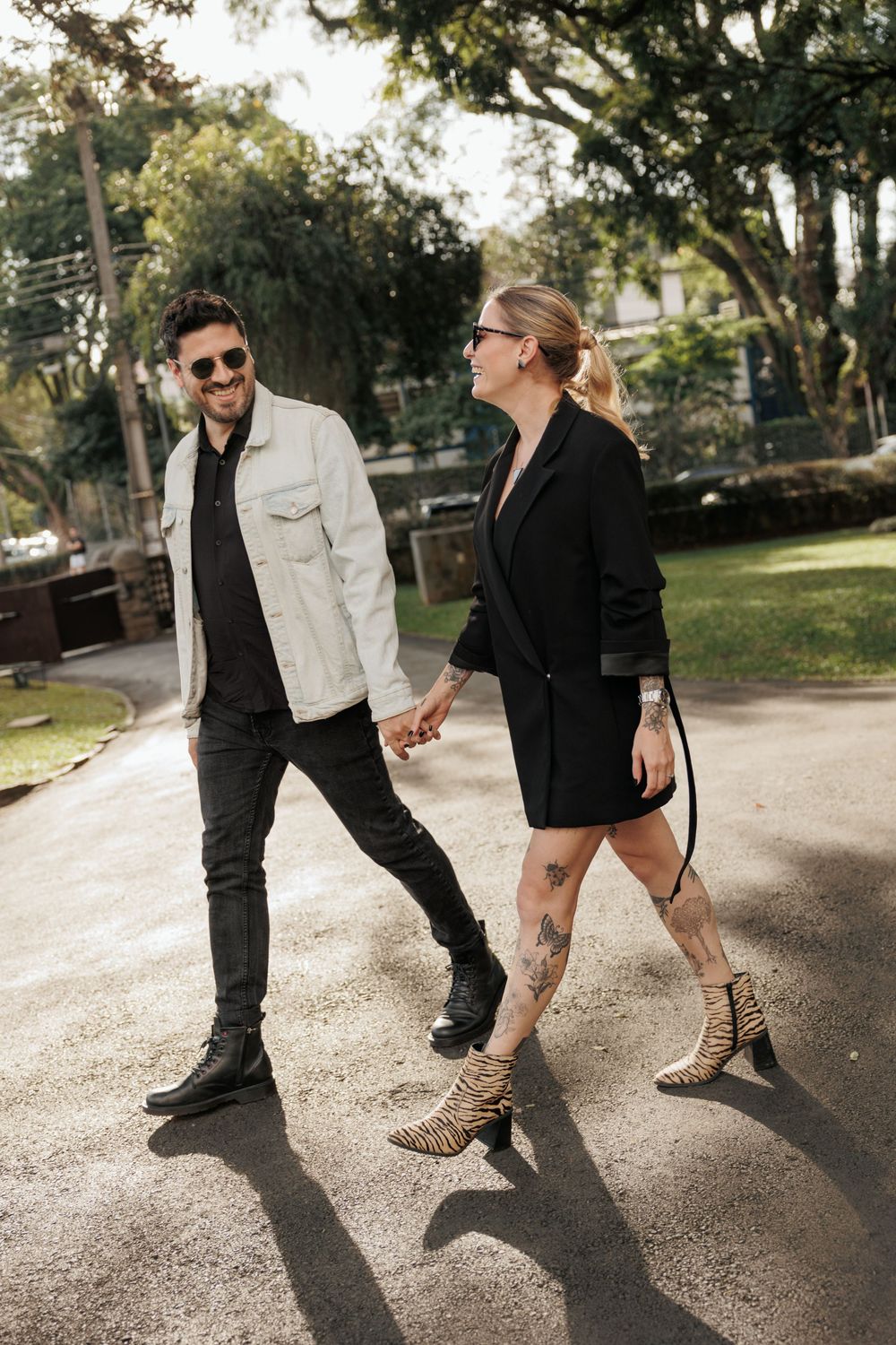 Stylish couple walking outdoors in sunlit park wearing contrasting black and white outfits with leopard print boots.