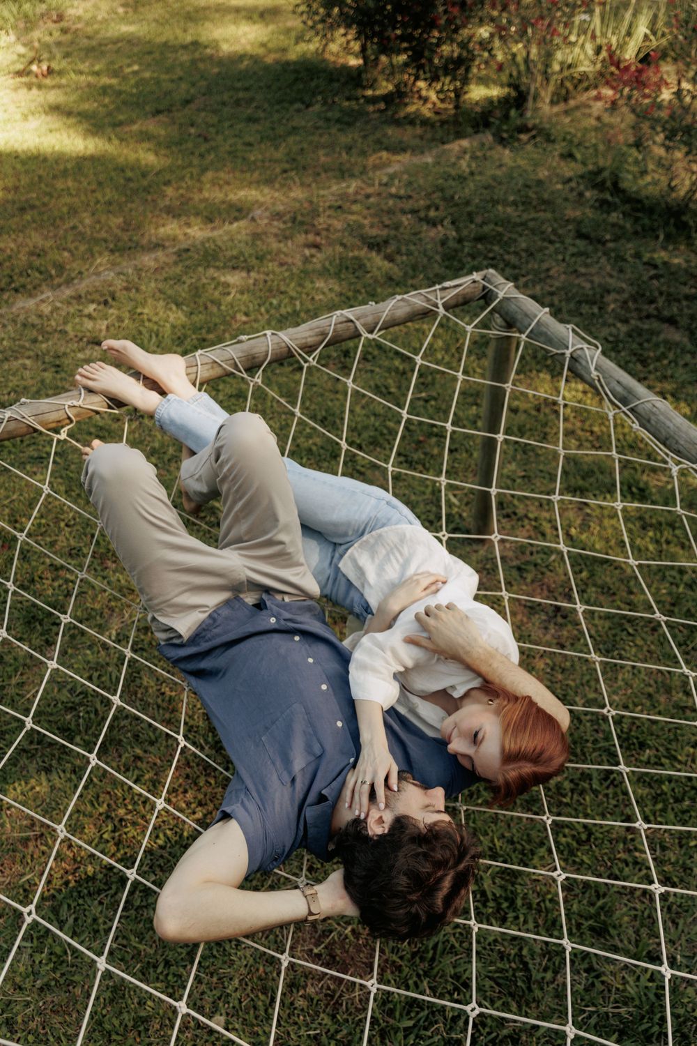 Couple laying together on wire hammock in sunny garden setting.