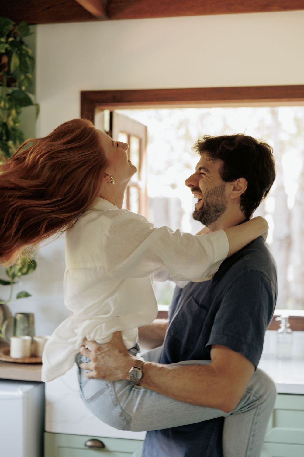 Intimate romantic moment captured in a sunlit kitchen setting.