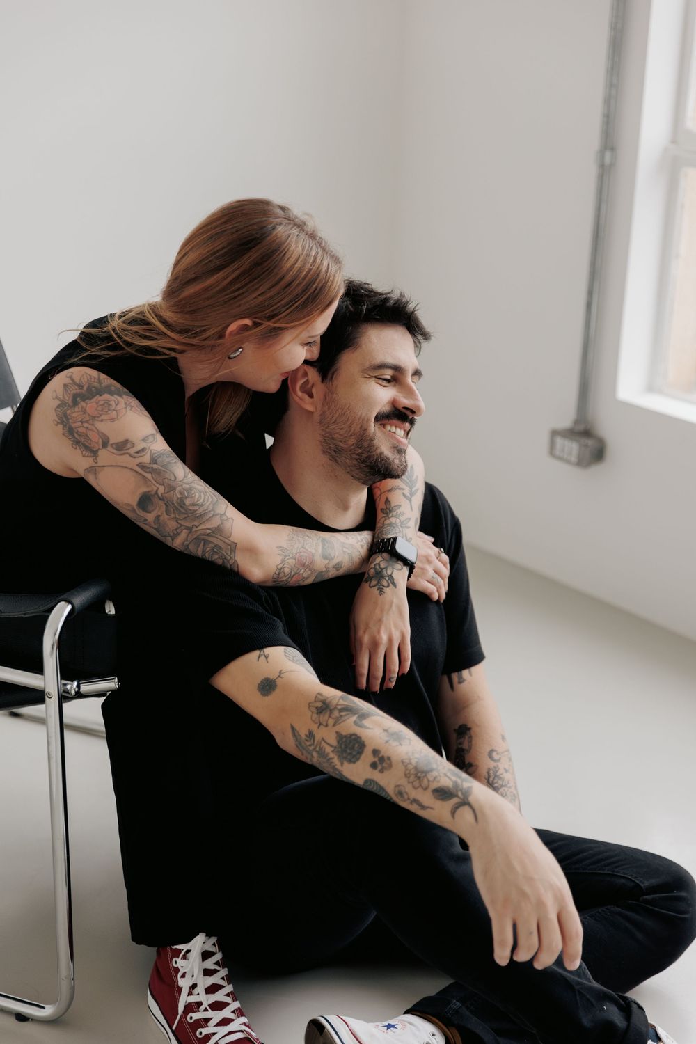 A couple sharing an intimate moment in a minimalist room with white walls and a casual relaxed vibe.