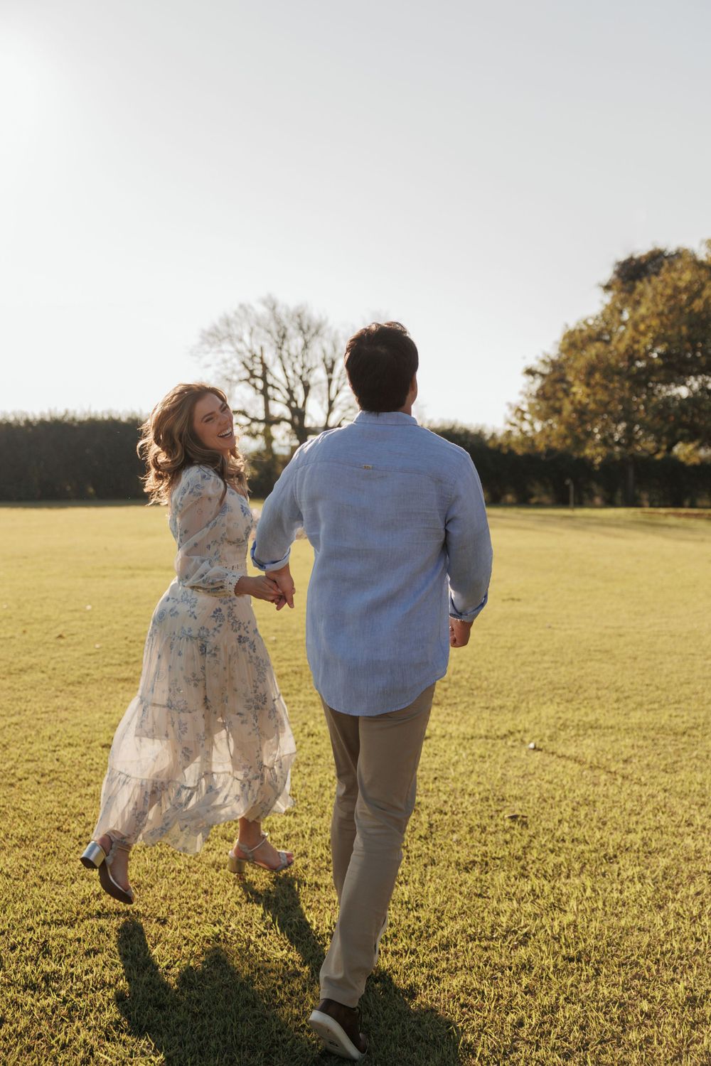 Romantic couple dancing together in a sunlit meadow at golden hour, with trees visible in background.