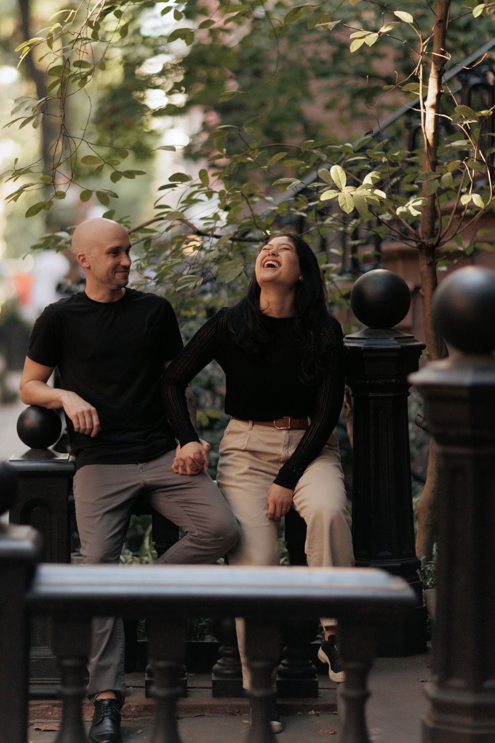 A candid moment of laughter shared between a couple sitting on a bench surrounded by greenery.