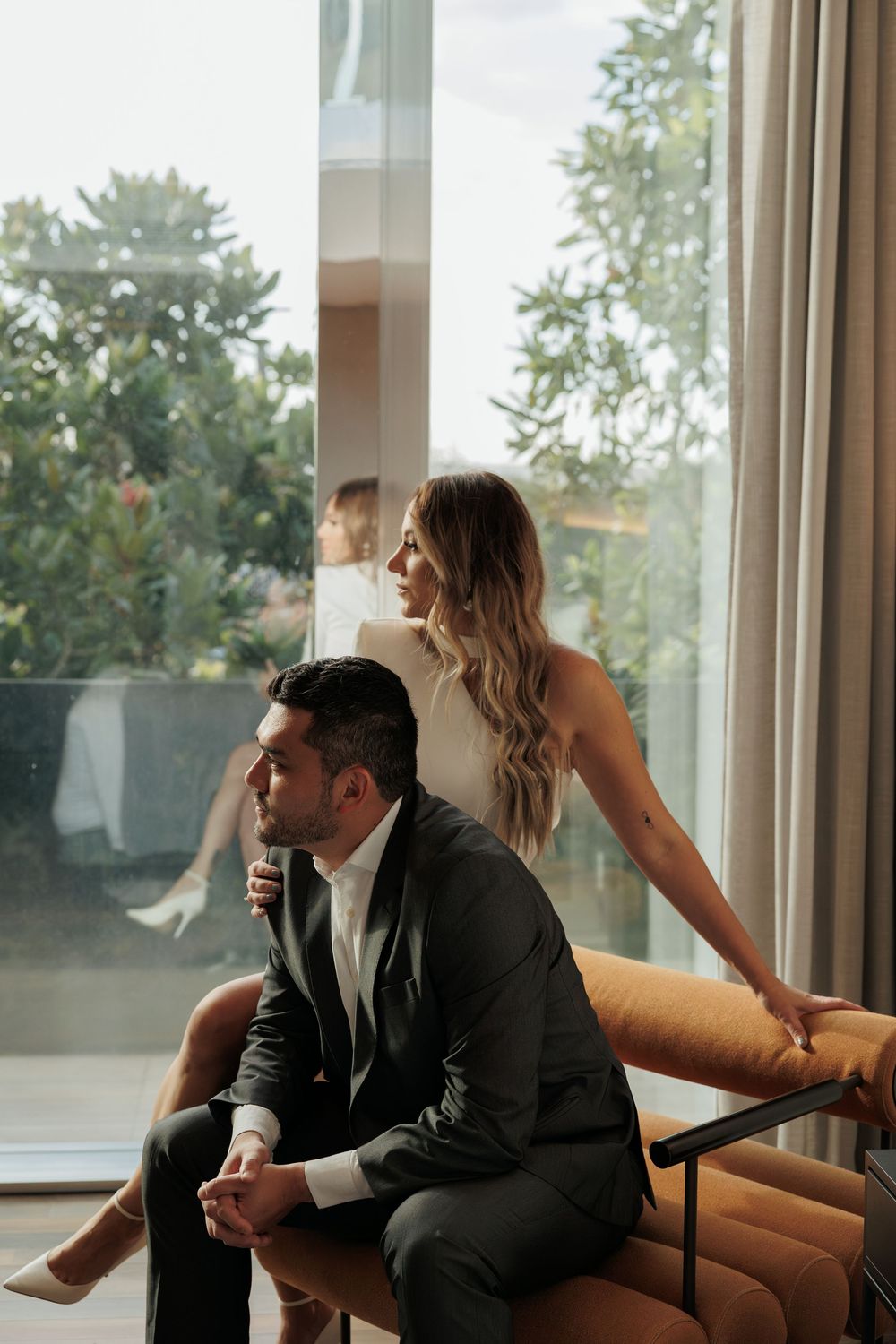 Elegant couple relaxing by large window with city view.