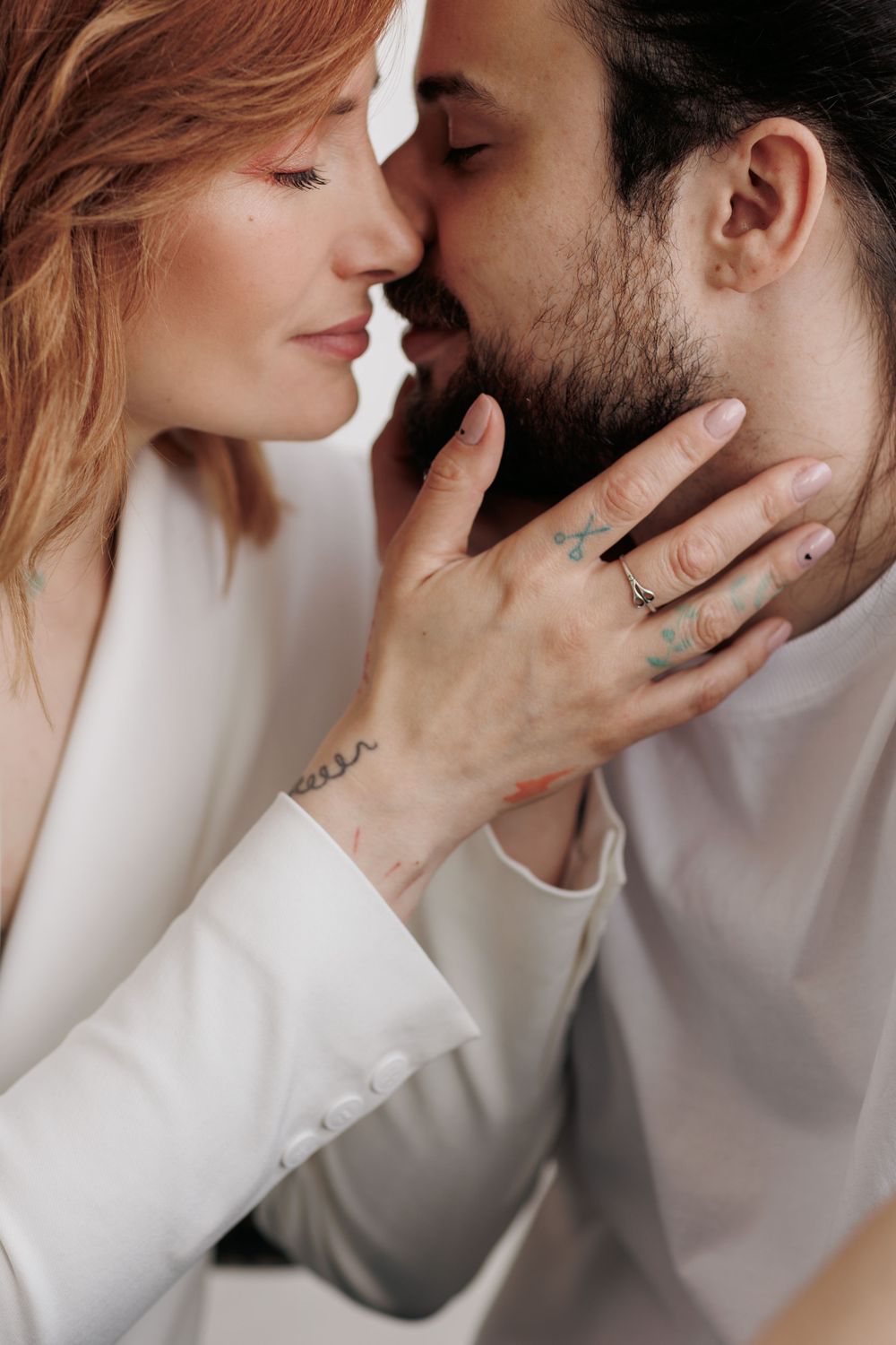 A romantic close-up shows an intimate couple in white clothing sharing a tender moment as she touches his face.
