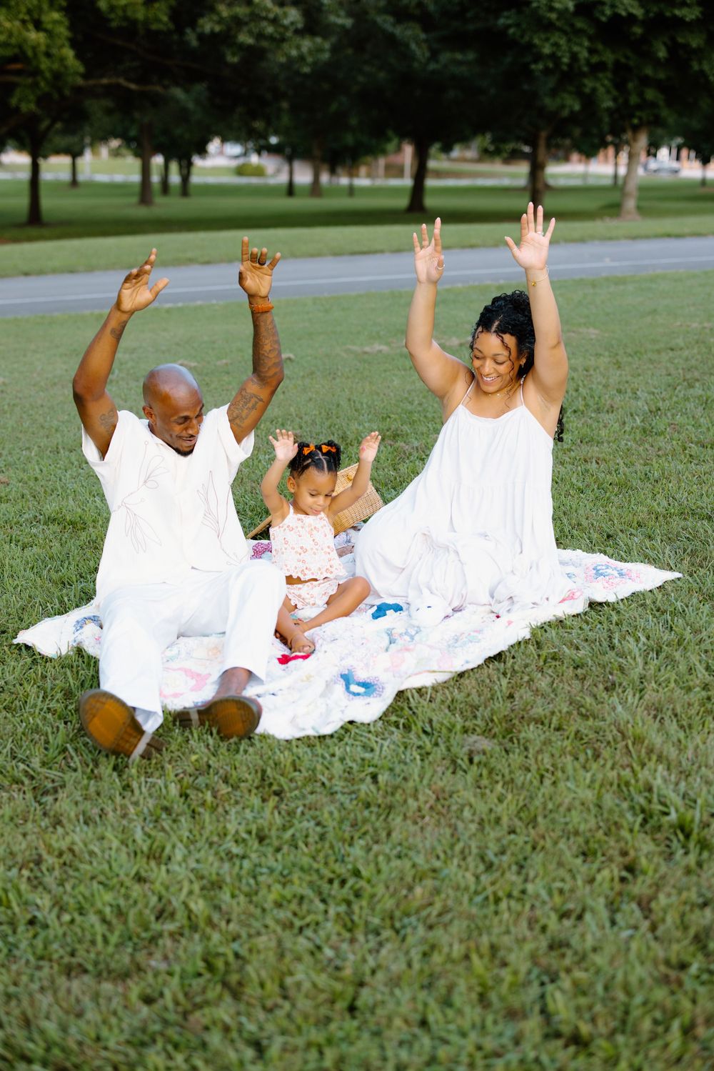 Family in white clothing having fun rolling on a blanket in a grassy park.