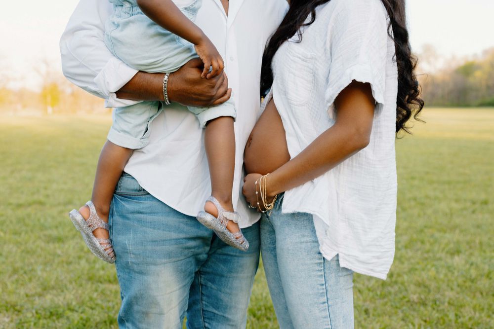 Couple in matching white shirts and jeans holding a small child in a candid outdoor setting.