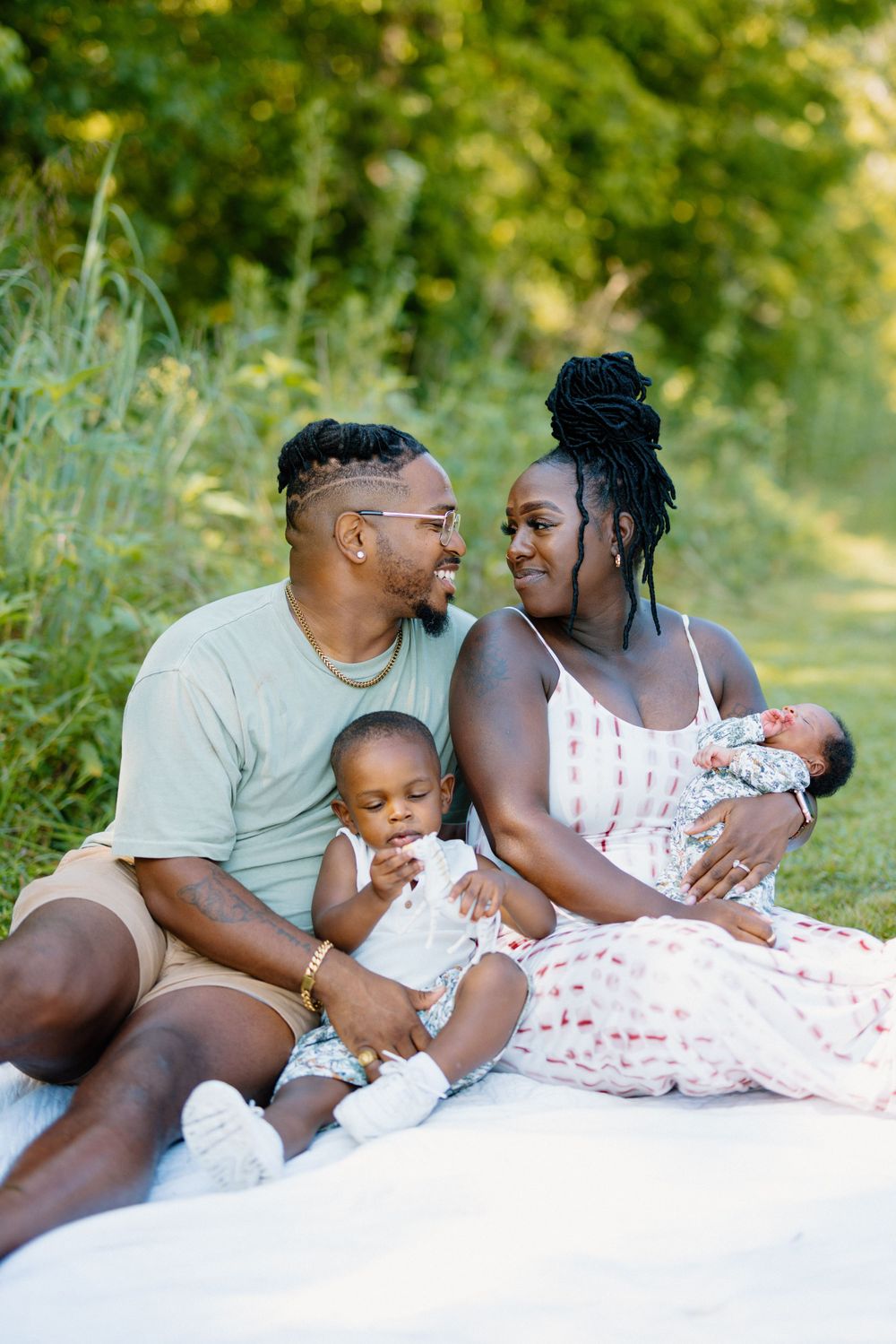 Family of four having a tender moment while relaxing outdoors on a blanket.