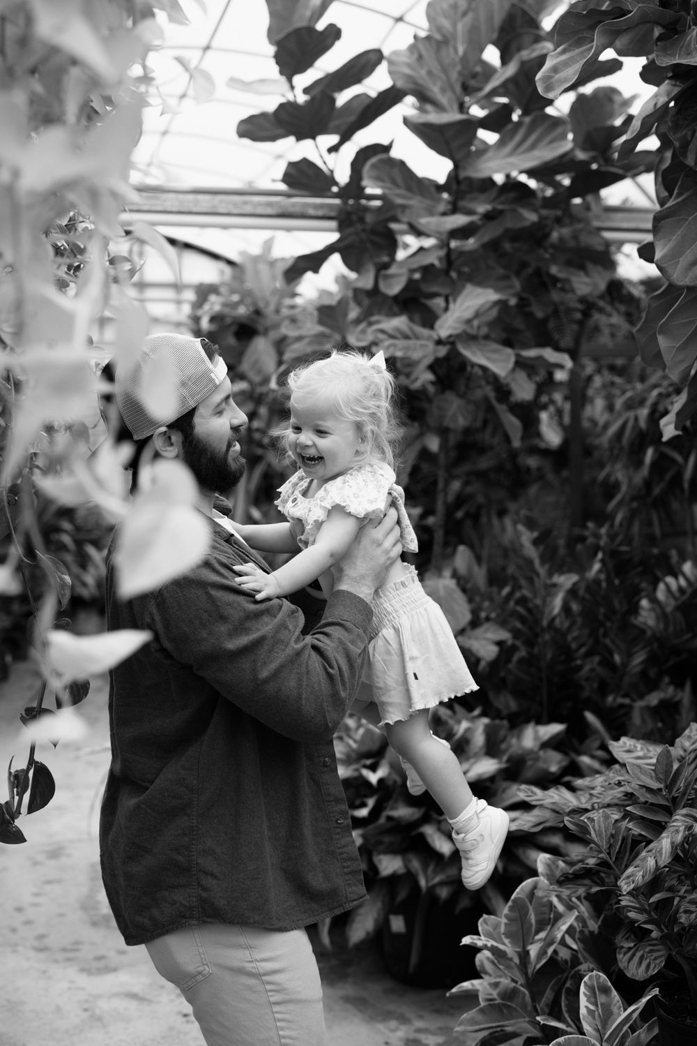 Black and white photograph of a tender moment between parent and child surrounded by lush garden foliage.