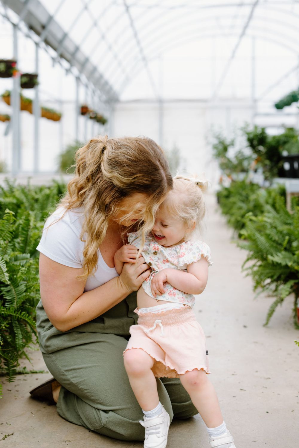 A tender moment shared between two people in a sunlit greenhouse surrounded by lush green ferns and plants.