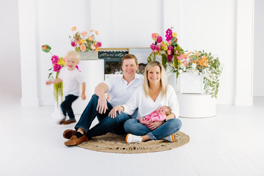 Beautiful spring family portrait session with bright floral arrangements on white backdrop and natural jute rug.