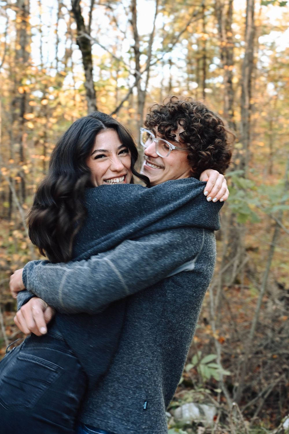 Two people embrace and laugh joyfully together in an autumn forest with golden leaves in the background.
