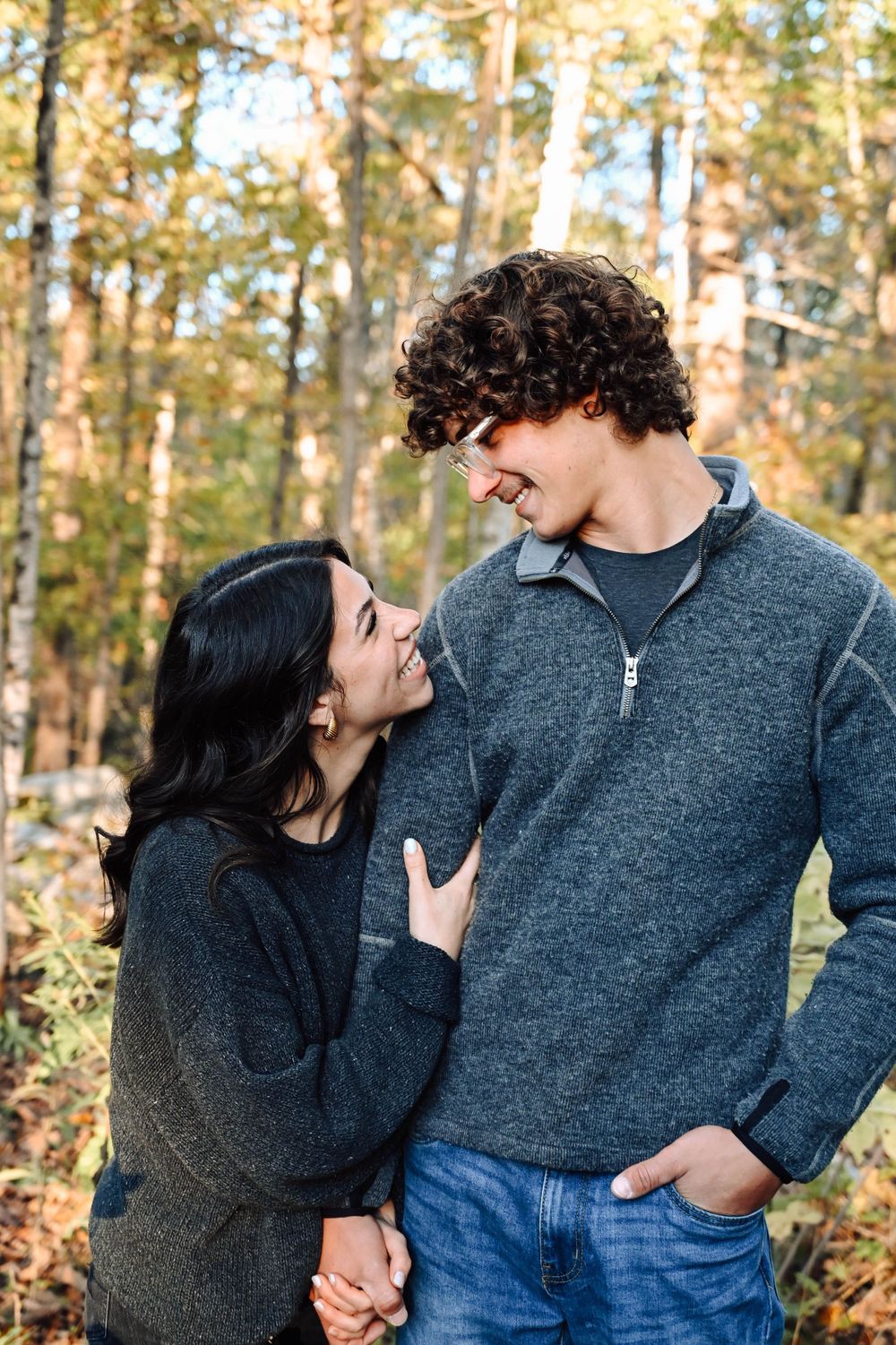 Couple in cozy sweaters share a tender moment while standing together in an autumn forest setting.