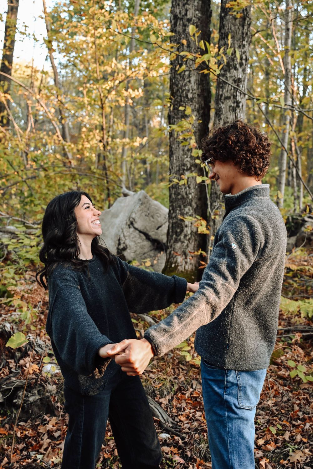 A couple hold hands and laugh together during an autumn day in the woods surrounded by yellow fall foliage.