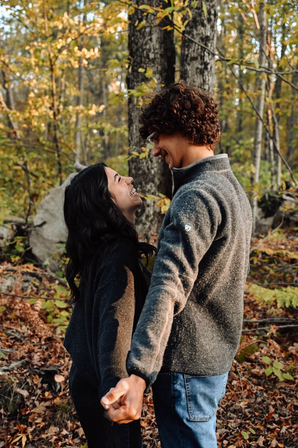 A romantic couple holding hands and gazing at each other in a beautiful autumn forest setting.