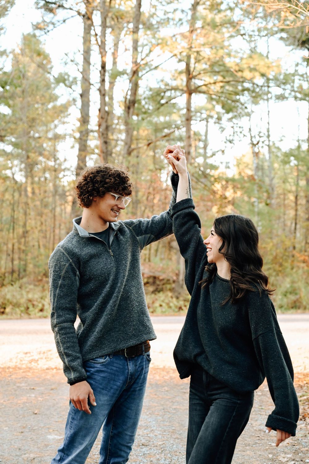 A joyful couple dancing together on a path in a golden autumn forest.