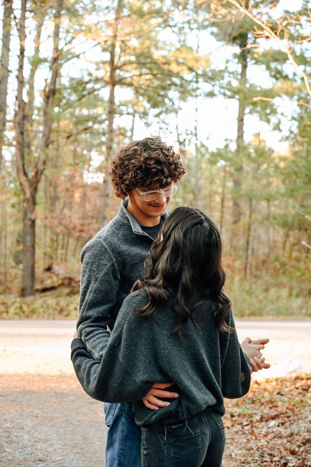 A couple in matching grey sweaters sharing a tender moment on an autumn forest path.