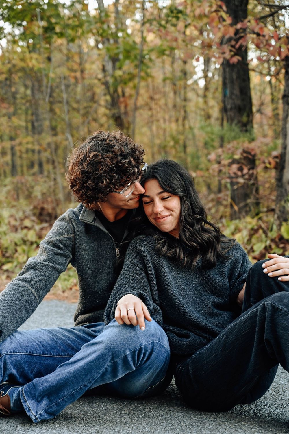 A couple in matching gray sweaters share an intimate moment while sitting on the ground during autumn.