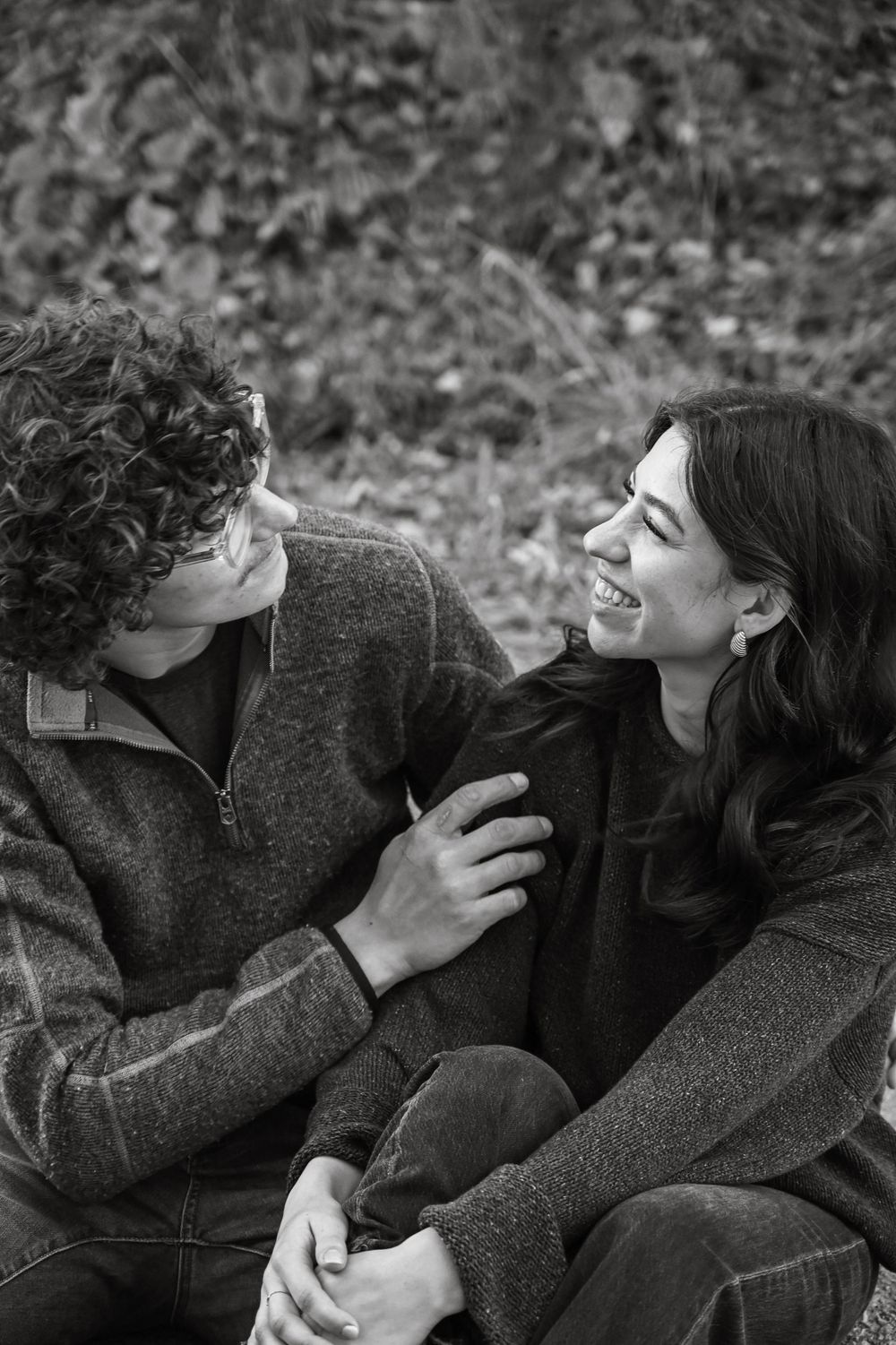 A romantic black and white photo of a couple laughing together while wearing cozy sweaters.