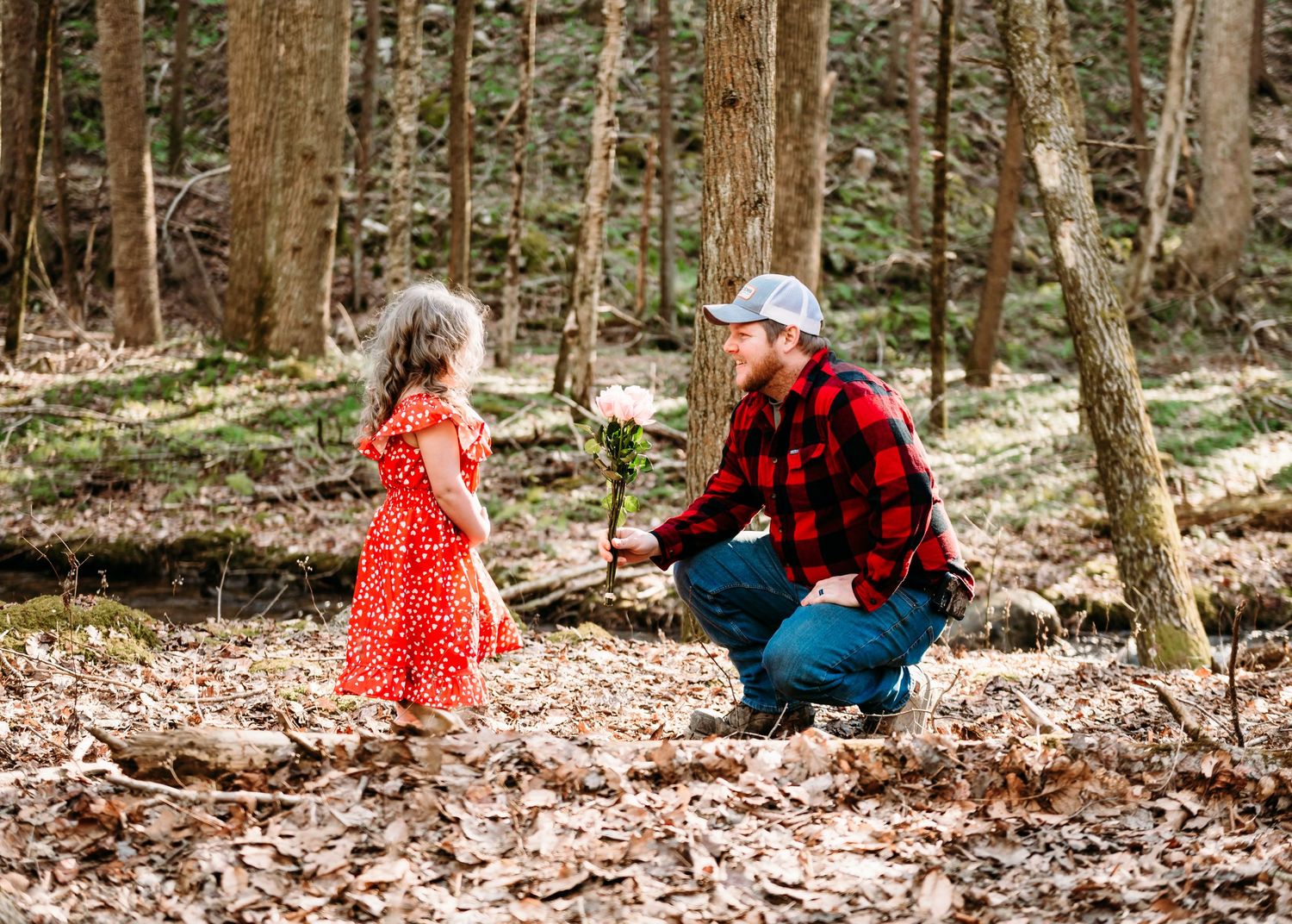 A touching moment captured in the woods with a bright red dress adding a pop of color to the scene.