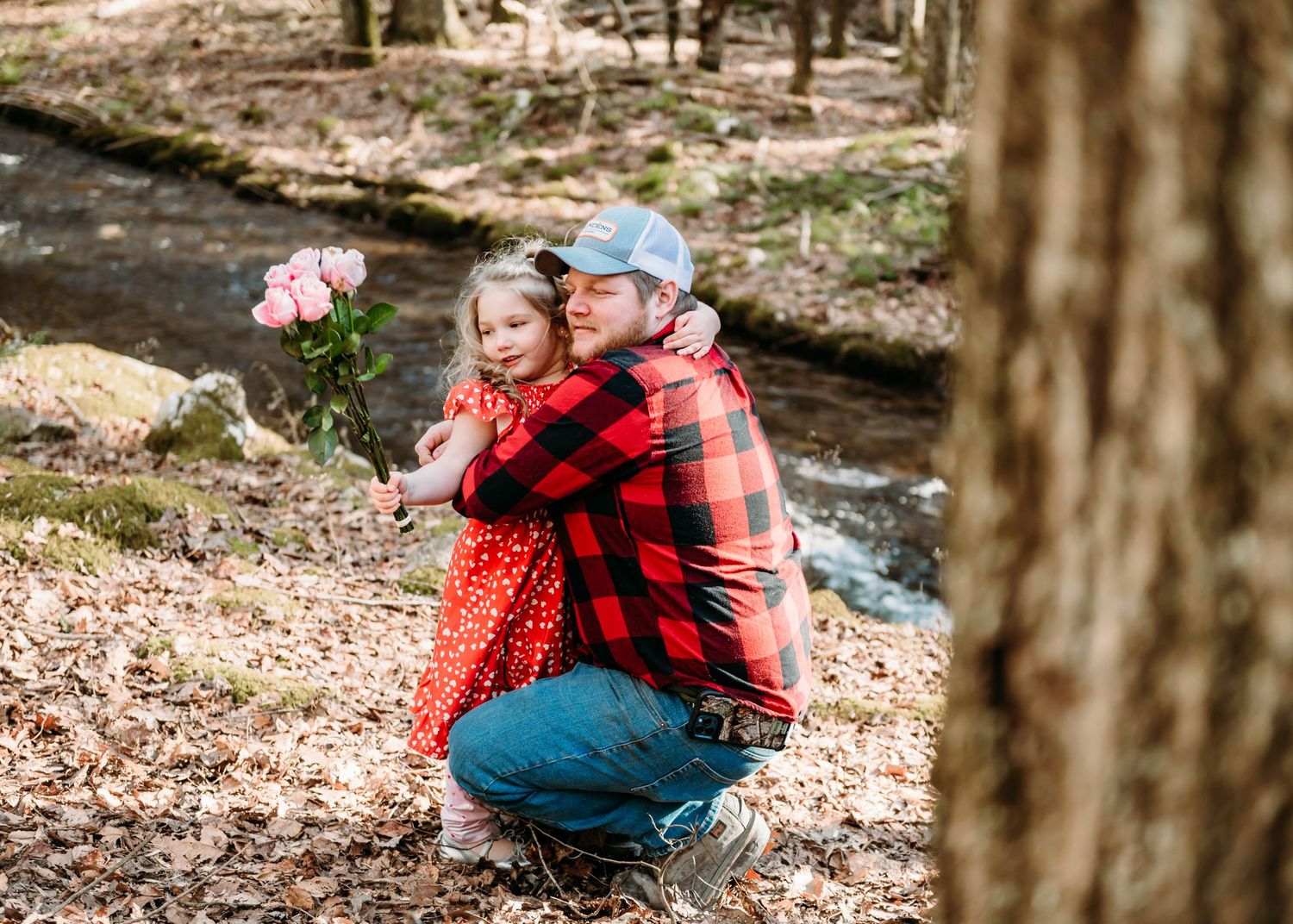 A tender moment shared in the woods with pink roses and a vibrant red dress. Father and daughter