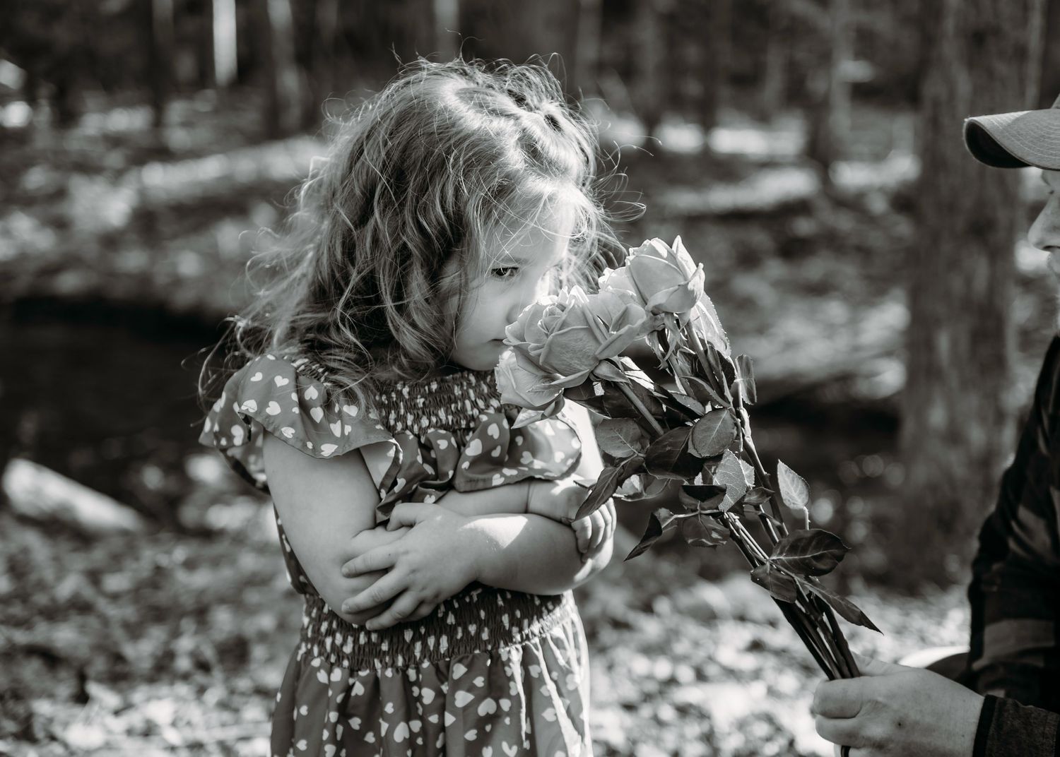 A black and white photo capturing a joyful moment with flowers in a forest setting.