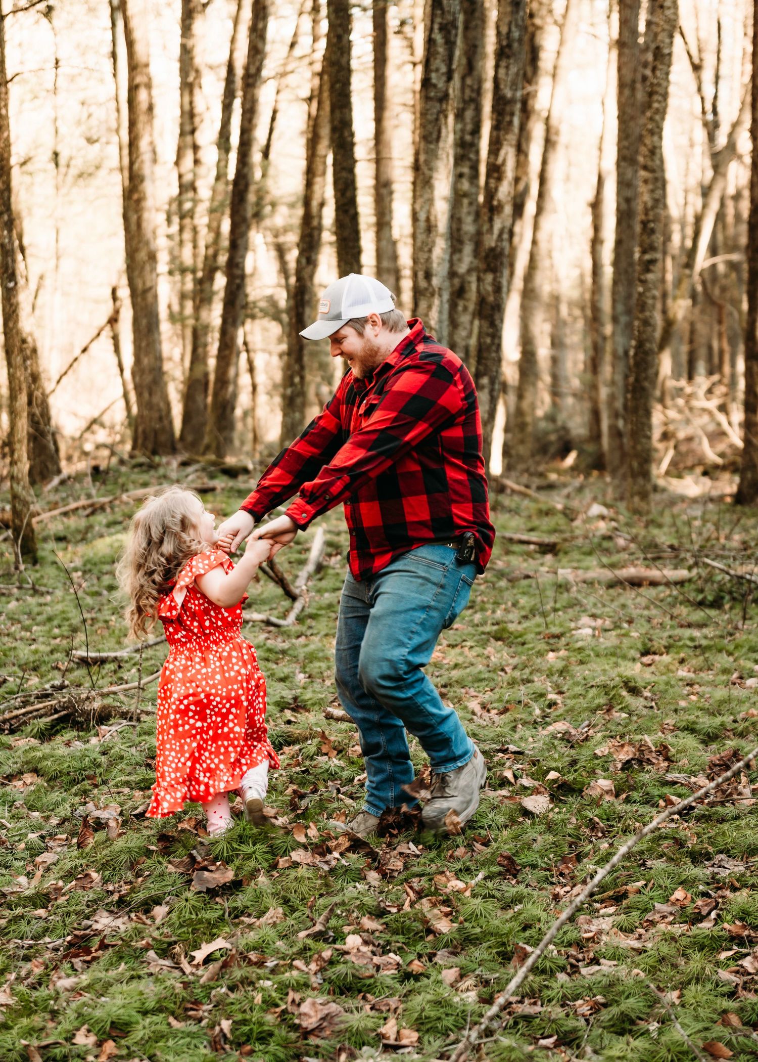 A playful dance moment in the woods with red dress and plaid creating a scenic forest portrait.