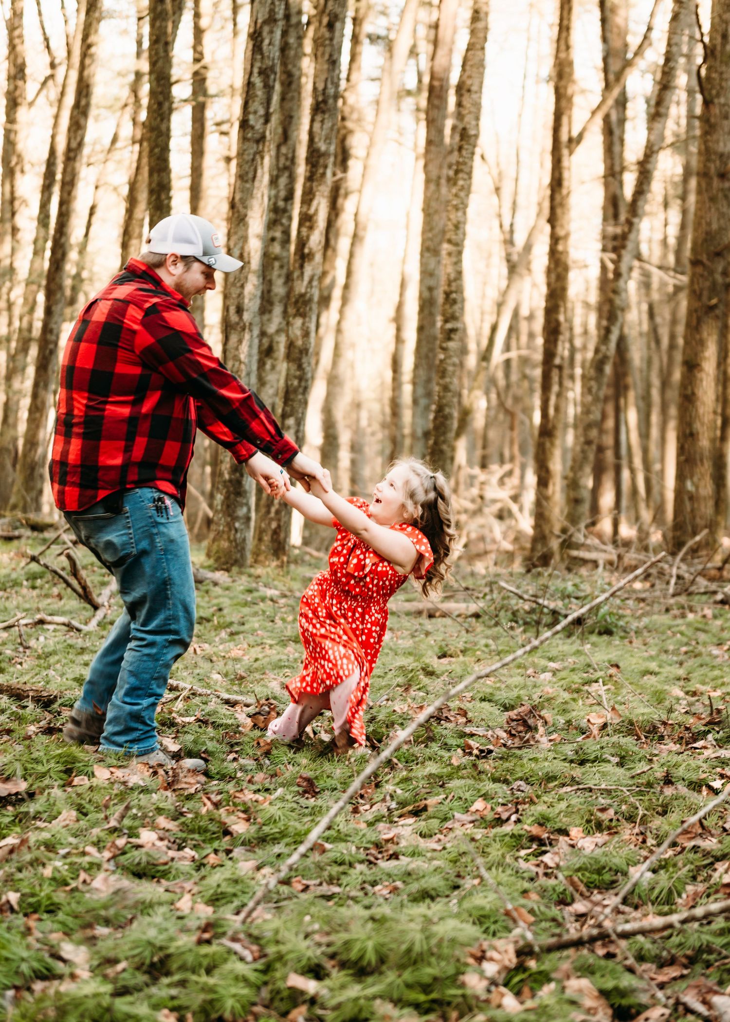 A joyful spin captured in the forest with father in red buffalo plaid and daughter in dress against autumn trees.