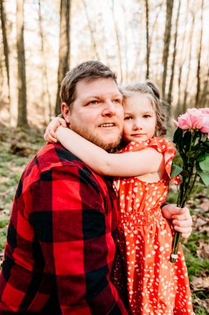 A touching outdoor portrait with red plaid and polka dots while holding pink flowers.