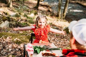 A joyful celebration in the woods with arms spread wide and flowers on a rustic table.