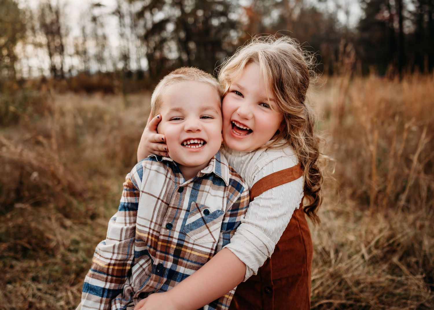 Two children share a joyful moment laughing together in a rustic autumn field during golden hour.