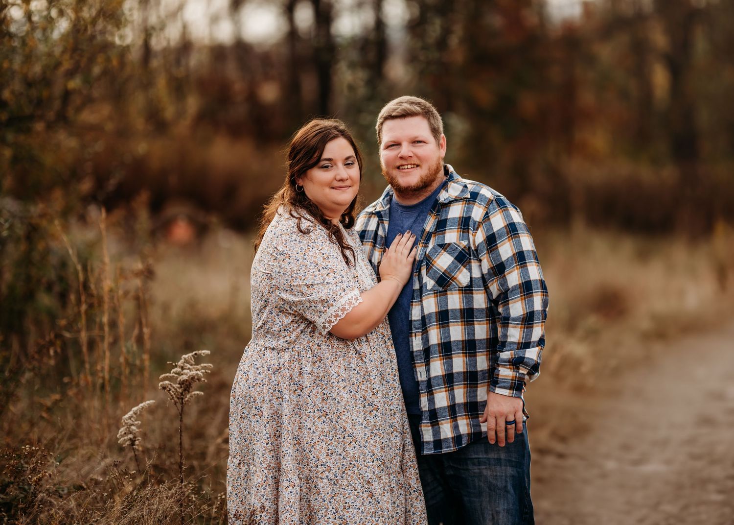 A loving couple embraces in a rustic outdoor setting with autumn foliage in the background.