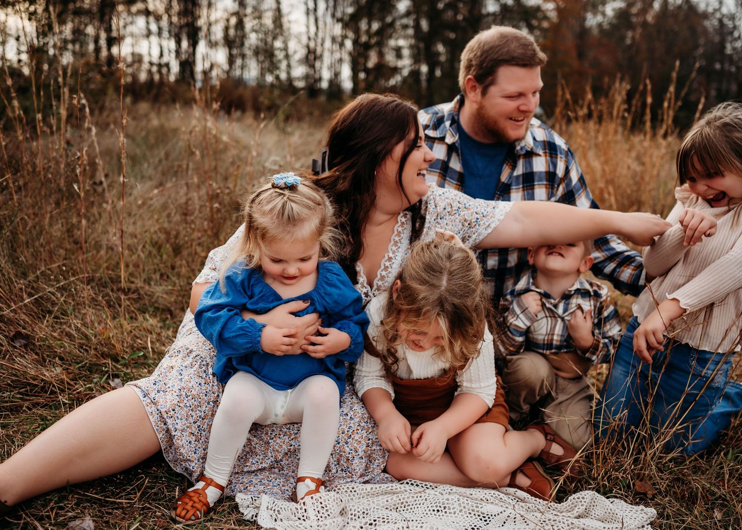 A family sits together on a blanket outdoors during golden hour in an autumn field.